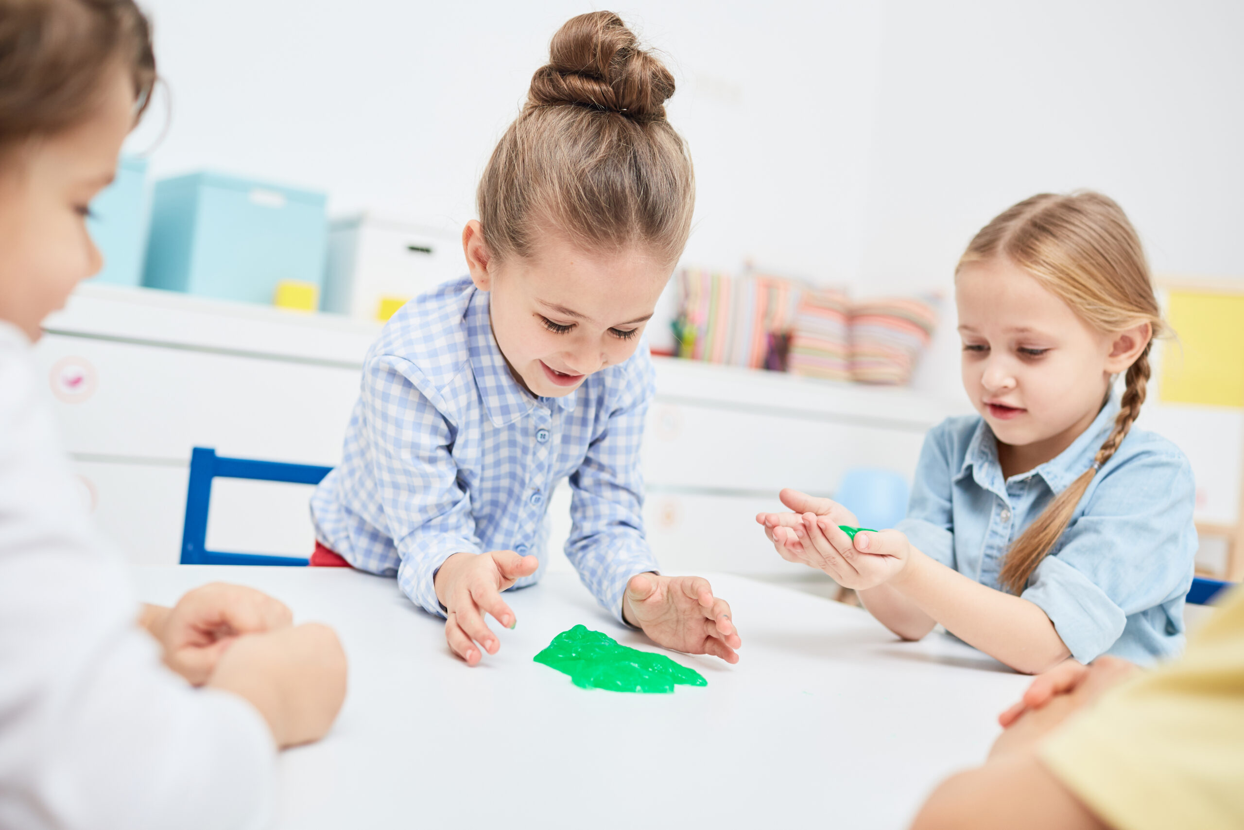 Adorable little girls playing with green funny slimes in kindergarten